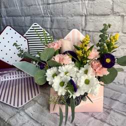 Mixed bouquet of white daisies, pink carnations, and purple flowers in a pastel gift box