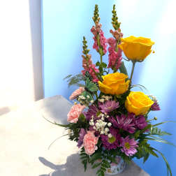 Bouquet of yellow roses, purple daisies, and pink snapdragons in a floral container
