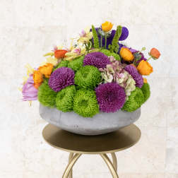 Colorful flower arrangement in a gray bowl vase on a gold stand