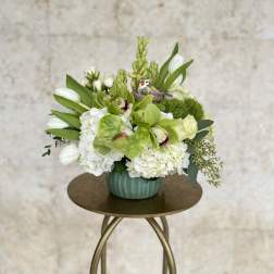 White and green floral arrangement in a teal vase with a small bird ornament