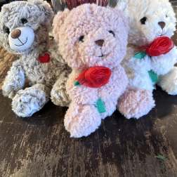 Three plush teddy bears with ribbon roses sit on a table.