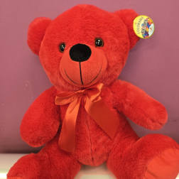 Bright red teddy bear with satin bow sitting against a purple background
