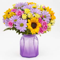 Mixed bouquet of sunflowers, daisies, roses, and carnations in a purple vase