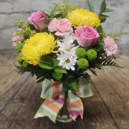 Pink roses and yellow chrysanthemums in a glass vase with a striped ribbon