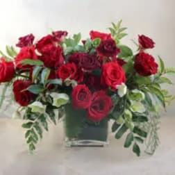 Red rose arrangement in a square vase with trailing greenery