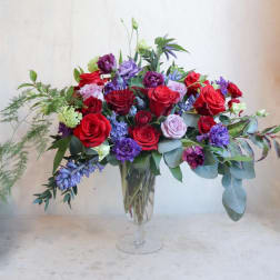Mixed bouquet of red, purple, and pink roses in a clear glass vase
