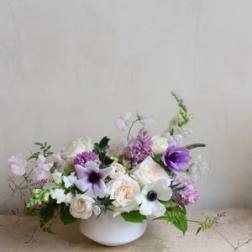 Low floral arrangement in a white bowl with white and purple blooms