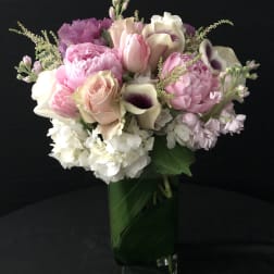Tall arrangement of pink and white flowers in a clear glass vase lined with green leaves.