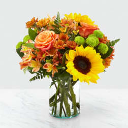 Bouquet of sunflowers, roses, and orange flowers in a glass vase