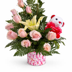 Pink roses and a yellow lily in a pink patterned vase with a teddy bear