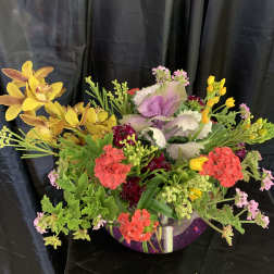 Mixed floral arrangement in a clear glass bowl with yellow orchids and pink blooms