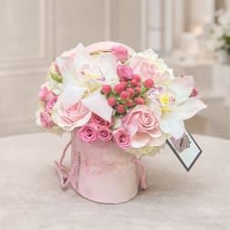 Pink and white floral arrangement in a pink hatbox with a tag
