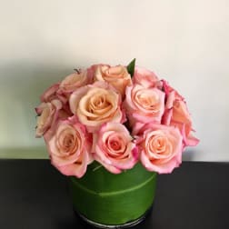 Pink and peach roses arranged in a green round box