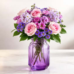Pink roses and purple mixed flowers in a purple glass vase
