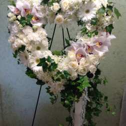 Heart-shaped white floral wreath on a stand with trailing ivy