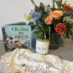 Flower arrangement beside a children’s book, candle, and baby onesie