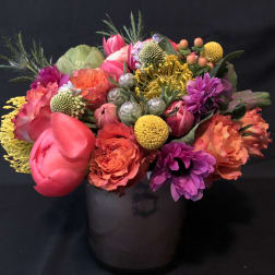 Bright mixed arrangement of pink, orange, yellow, and purple flowers in a smoky glass cylinder vase