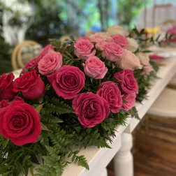 Elongated centerpiece of hot pink and light pink roses running along a white table.