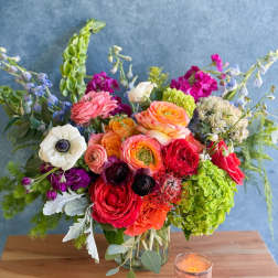 Colorful mixed flower arrangement in a glass vase with a candle beside it