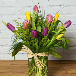Colorful tulips arranged in a glass vase with a raffia bow