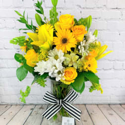 Yellow and white flower arrangement in a glass vase with a striped ribbon