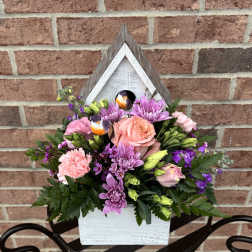 Mixed pink and purple flowers arranged in a white wooden birdhouse planter