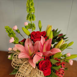 Bouquet of pink lilies and red roses with green filler in burlap wrap