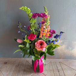 Tall mixed bouquet in a glass vase with pink, purple, blue, and peach flowers
