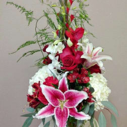 Tall red, white, and pink flower arrangement with lilies, roses, orchids, and hydrangeas in a clear glass vase.