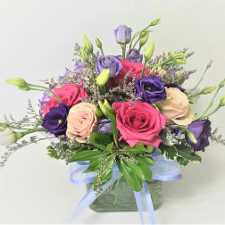 Pink, purple, and cream flowers in a glass vase with a blue ribbon
