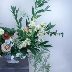White and blush flowers in a white pedestal vase with tall greenery