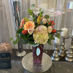 Mixed bouquet in a purple vase with candles and a gift box nearby