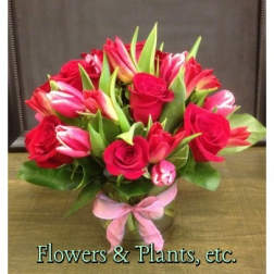 Bouquet of red roses and pink tulips in a glass vase with a pink ribbon
