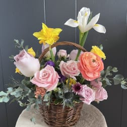 Basket arrangement with pink roses, yellow daffodils, and white iris