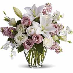 Bouquet of white lilies, pink roses, and pale purple flowers in a glass vase