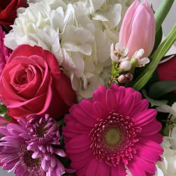 Close-up of a bright bouquet with hot pink gerbera daisy, pink and red roses, white hydrangeas, and a pale pink tulip