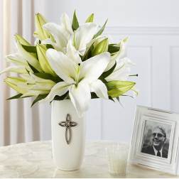White lilies arranged in a tall white vase beside a framed photo