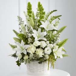 White lilies and roses arranged in a white basket with tall greenery.