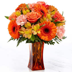 Orange and pink mixed bouquet in an amber glass vase