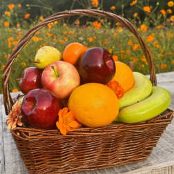 Wicker basket filled with assorted fresh fruits and a few orange blossoms on a rustic wooden surface