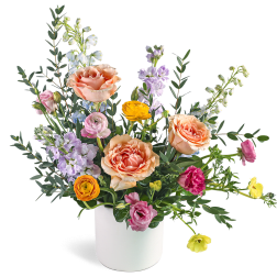 Mixed arrangement of peach roses, ranunculus, and lavender blooms in a white vase