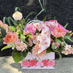 Pink and peach flower arrangement in a decorative gift bag with a floral ribbon
