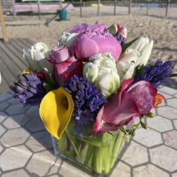 Mixed bouquet with pink roses, white tulips, purple hyacinths, and a yellow calla lily in a glass vase
