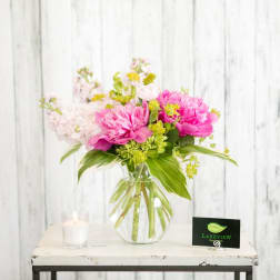 Pink peonies and pale blossoms in a clear glass vase with a candle nearby