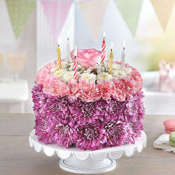Pink floral cake with striped birthday candles on a white stand