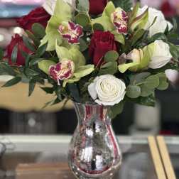 Red and white roses with green orchids in a mirrored vase