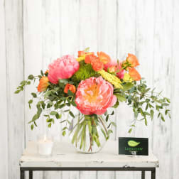 Pink and orange floral arrangement in a clear glass vase with a candle beside it