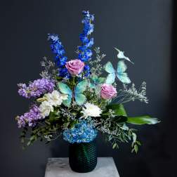 Tall floral arrangement with blue, purple, and white flowers in a dark vase
