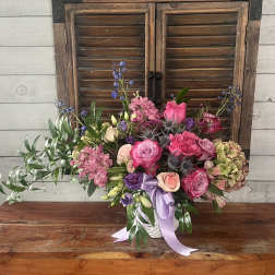 Pink and purple mixed flower arrangement in a white container with ribbon