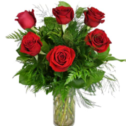 Red roses arranged in a clear glass vase with green foliage